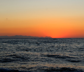 the sun setting behind the promontory with the sea in the foreground