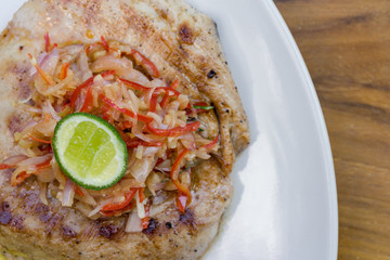 Close up photo of fish steak with chopped chilli & a slide of lime.