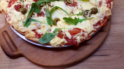 Tasty vegetarian pizza with olives, arugula, mozzarella and  cherries on a wooden table.