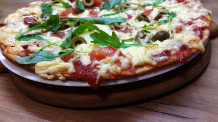 Tasty vegetarian pizza with olives, arugula, mozzarella and  cherries on a wooden table.