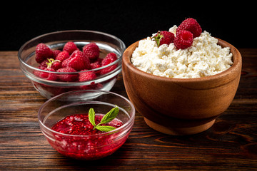 Cottage cheese, raspberry jam and fresh raspberry on dark wooden background.