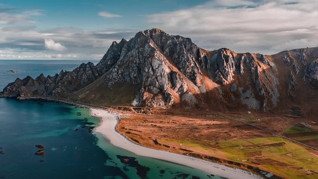A hyperlapse video. Mountain ridge of Royken on the Andoya, Norway. Beautiful sandy beach and clear blue waters, thin white clouds passing above, a stripe of a road following the coastline.