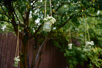 Rustic wedding decorations with flowers in glass jar hanging on green tree outdoors, copy space. Floral arrangement. Wedding concept