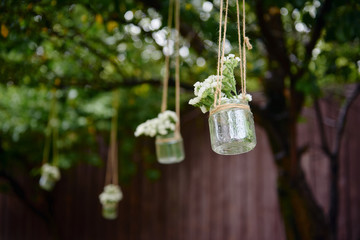 Rustic wedding decorations with flowers in glass jar hanging on green tree outdoors, copy space. Floral arrangement. Wedding concept