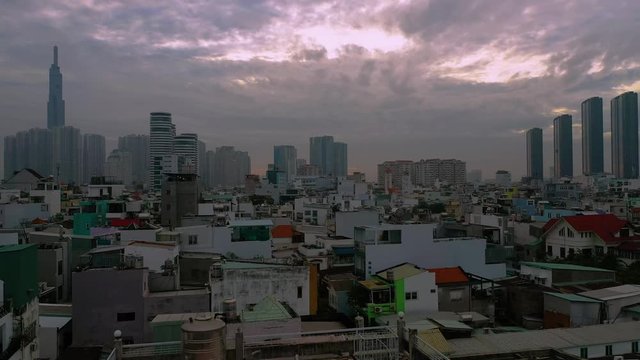 Sunrise drone flying low and backwards over densely populated residential area in Southeast Asia featuring traditional buildings and new development of high rise buildings