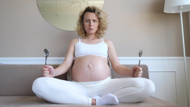 Hungry Dissatisfied Pregnant Woman Holding Spoon And Fork In Hands Waiting For Food.