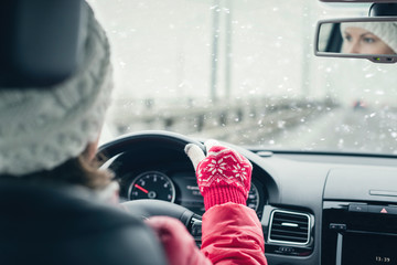 Woman in the red jacket, hat and christmas gloves is driving on the highway at the winter snowfall.  View from the back seat of the car. concept. - 310397466