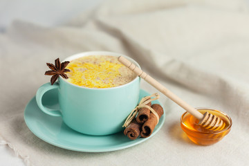 Golden Milk, turmeric latte made with honey,curcuma and other spices: cinnamon, anise. Healthy hot winter drink, natural and organic beverage. Close up, front view. Blue mug, neutral white background