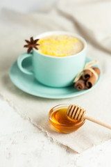 Golden Milk, turmeric latte made with honey,curcuma and other spices: cinnamon, anise. Healthy hot winter drink, natural and organic beverage. Close up, front view. Blue mug, neutral white background
