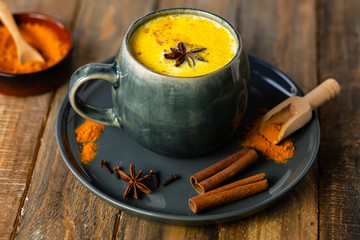 Golden milk in grey mug, turmeric latte made with curcuma and other spices: cinnamon, anise. Healthy hot winter drink, natural, organic beverage. Close up, front view. Dark wooden rustic background
