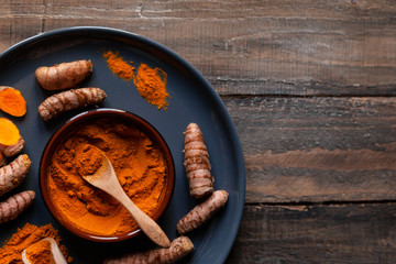 Grey plate with bright orange curcuma powder and fresh turmeric roots. Alternative indian medicine, also spicy ingredient for oriental cuisine. Rustic wooden background, close up, top view, copy space