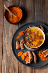Golden milk in white mug, turmeric latte made with curcuma and other spices: cinnamon, anise. Healthy hot winter drink, natural, organic beverage. Close up, front view. Dark wooden rustic background