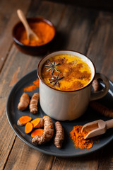Golden milk in white mug, turmeric latte made with curcuma and other spices: cinnamon, anise. Healthy hot winter drink, natural, organic beverage. Close up, front view. Dark wooden rustic background