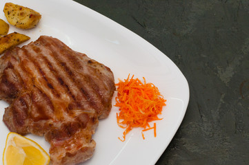 Grilled meat steak with lemon, carrots, lettuce and potatoes. Juicy and very tasty dish of Italian cuisine