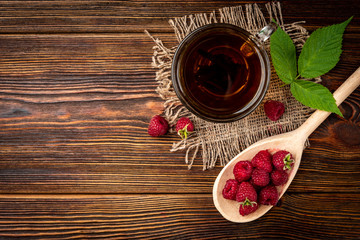 Fototapeta na wymiar Cup of black tea and raspberry on dark wooden background.