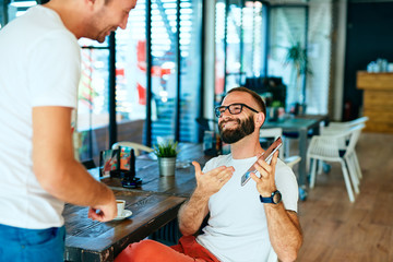 Attractive bearded man with glasses in a cafe working on laptop and chatting with a friend	