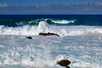 Fototapeta premium Olas grandes rompiendo contra las rocas de la costa y cielo parcialmente nublado