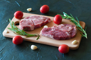 Pork steaks raw, red tomatoes, rosemary and garlic on a cutting board