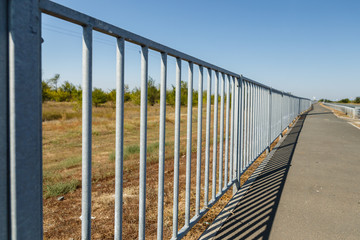 metal fence between the field and the pedestrian walkway, highway