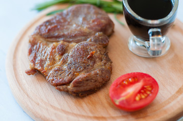 Cooked, grilled pork steak on a wooden round board, with soy sauce, rosemary and tomato