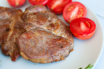 Tasty, juicy, fried meat steaks of pork or beef with sauce, spices and tomato on gray plate, on a light wooden background, top view