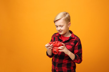 Young boy with a camera. Young handsome smiling caucasian boy in the red shirt on the yellow background. Horizontal, straight on.