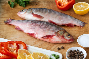 Raw roach fish with lemon and pepper on a wooden background