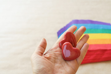 Two hearts lying in female hand and background stack of napkins painted under a rainbow on craft paper. Valentine's day concept and lgbt. Natural materials and zero waste