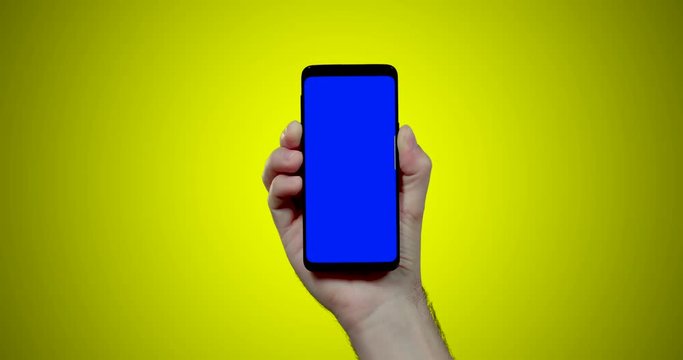 man's hand holding smartphone with blue croma key on yellow background click touch three times 