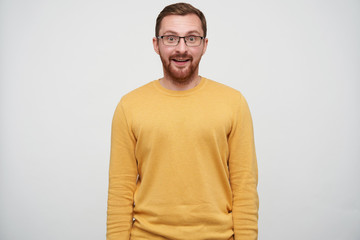 Suprised young brown haired pretty guy with beard wearing casual pullover and glasses while...
