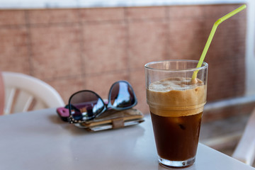 Ice cold Greek frappé with a purse and sunglasses of focus in background