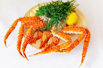 Shrimp, crab, lemon and greens on a plate on a white background.