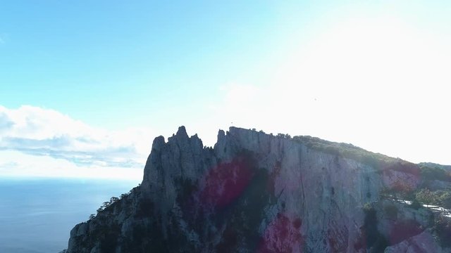 Aerial of steep mountains and funicular with people standing on the edge. Shot. Breathtaking seascape with rocks and blue cloudy sky on the background.