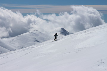 esquiador subiendo la ladera de una montaña nevada con nubes al fondo