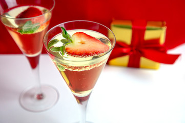 Two champagne glasses with heart shaped strawberry and a gift in the background Valentine's Day concept