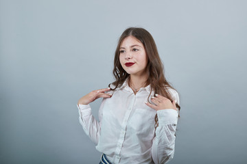 Cheerful caucasian woman over isolated gray background holding hands on shoulder, looking aside, smiling wearing casual white shirt