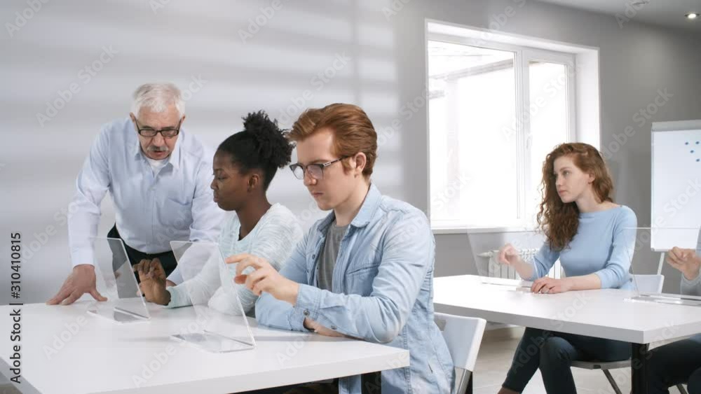Poster medium shot of multinational students sitting in classroom and working on task on transparent intera