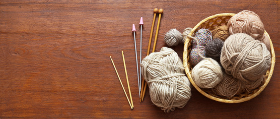 Top view of a wicker basket with balls of wool yarn for hand knitting and a set of hooks and...