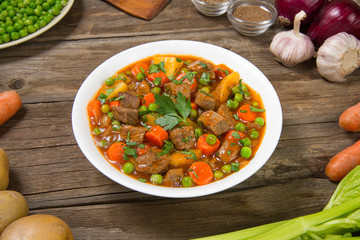 Slow cooker beef stew in a white plate on a old rustic wooden table. Selected focus