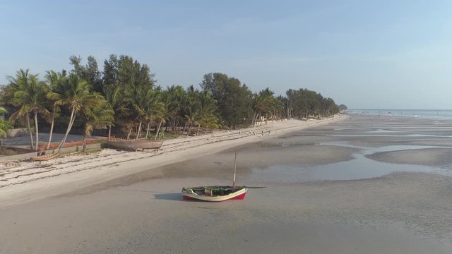 Aerial push in then circle pan of local people cleaning African tropical beach