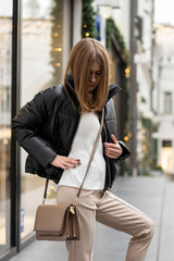 portrait of a european young model in a warm leather jacket oversized with beige textile pants with...