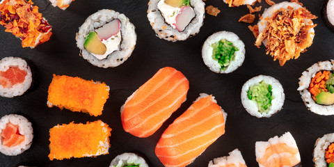 Large sushi set, a close-up panorama, shot from above on a black background. An assortment of various maki, nigiri and rolls
