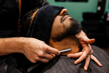 manos de barbero con navaja de afeitar estan afeitando y arreglando la barba de un chico...