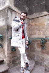 Stylish handsome man with a beard in a winter jacket with fur posing outdoors. Portrait of an elegant guy in beautiful clothes