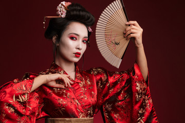 Image of young geisha woman in japanese kimono holding wooden hand fan