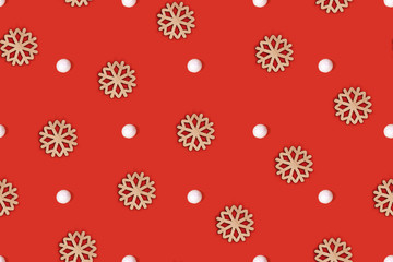 Simple seamless top view flat lay with wooden snowflake ornamenst and white snowballs arranged on bright red background