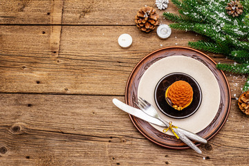 Christmas and New Year dinner place setting. Sweet snack, fir tree branch, candles, cones, ceramic plates, fork and knife. Winter cutlery wooden background