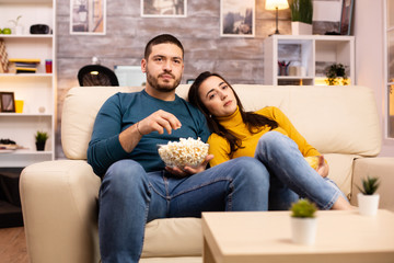 Obraz premium Handsome couple at home eating pop corn and watching TV