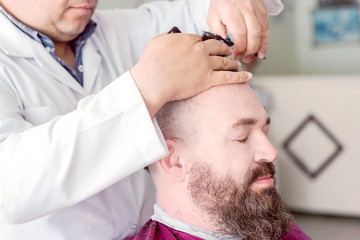 Barber makes a mohawk hairstyle of a adult bearded man .