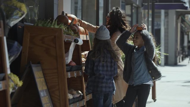 Mother and children examining pumpkins at food display on city sidewalk / San Francisco, California, United States